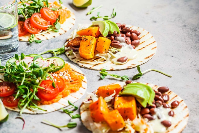 Open vegan tortilla wraps with sweet potato, beans, avocado, tomatoes, pumpkin and seedlings 