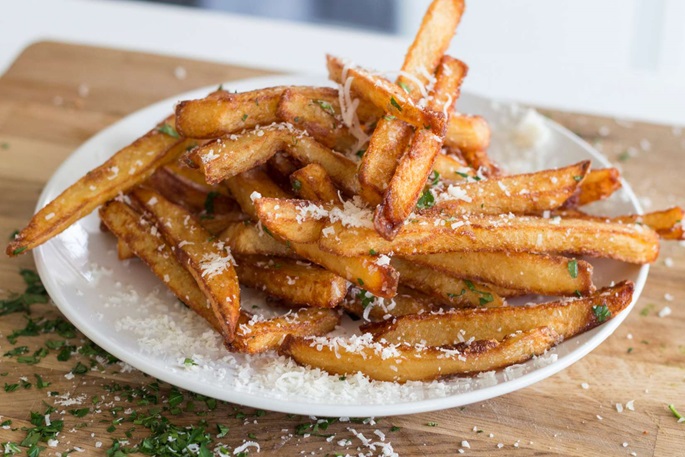 Crispy beef tallow-fried fries topped with parsley, Parmesan, and truffle oil on a wooden cutting board