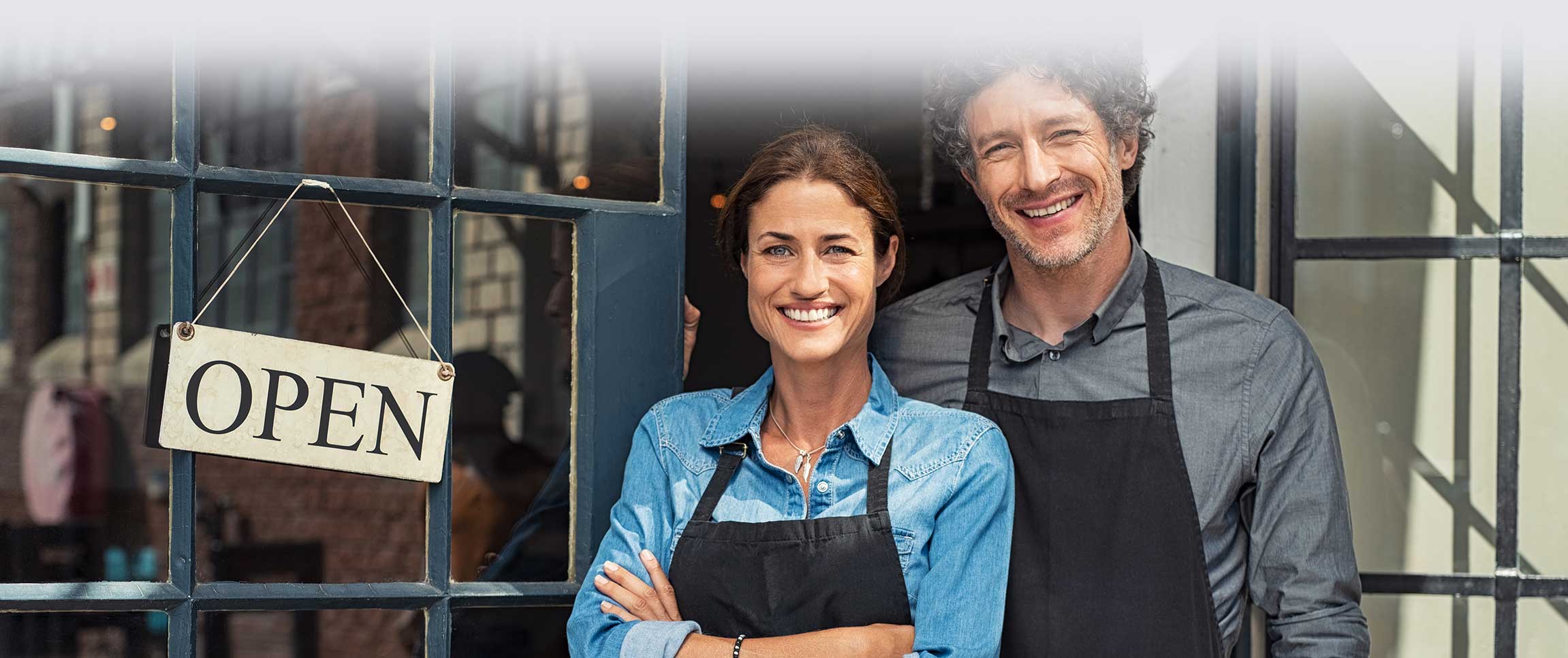 Two cheerful small business owners smiling and looking at camera while standing at entrance door.