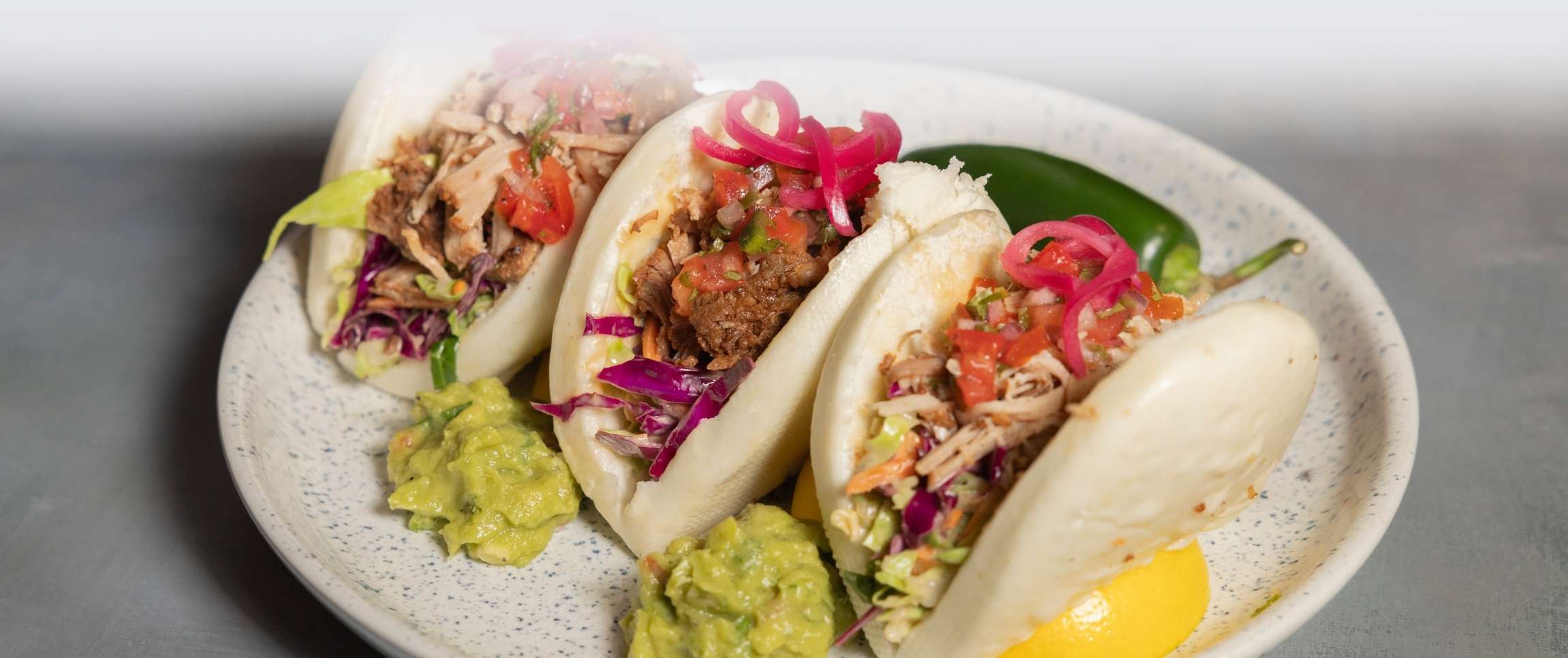 Birria Bao Buns with cilantro lime slaw, drizzled in roasted garlic chipotle aioli.