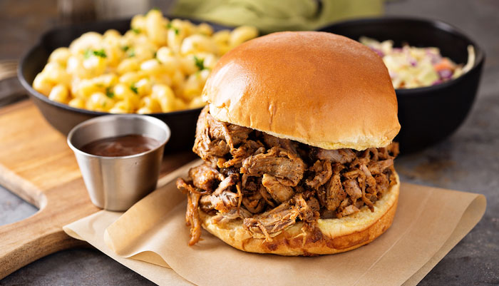 BBQ Sandwich on a cutting board with a side of cole slaw and mac and cheese